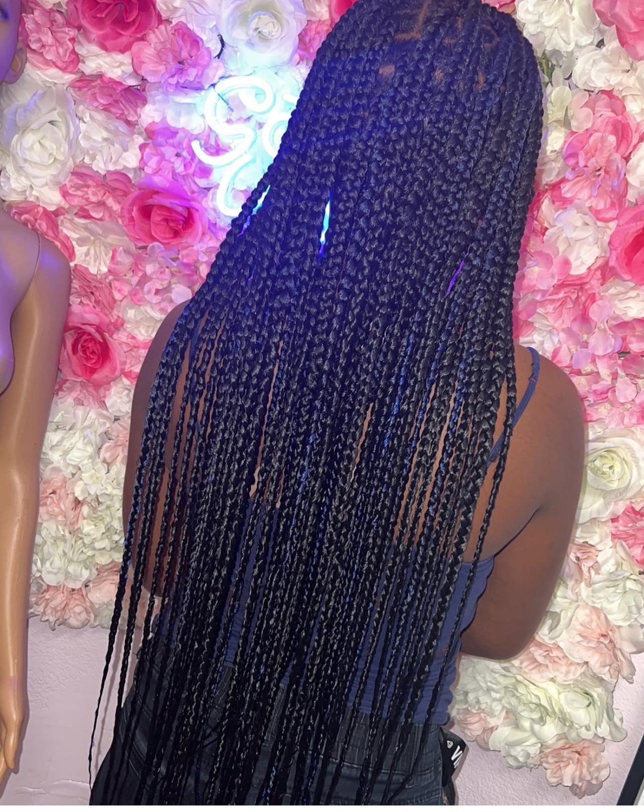 Long dark box braids with a neon 'Good Vibes' sign in the background