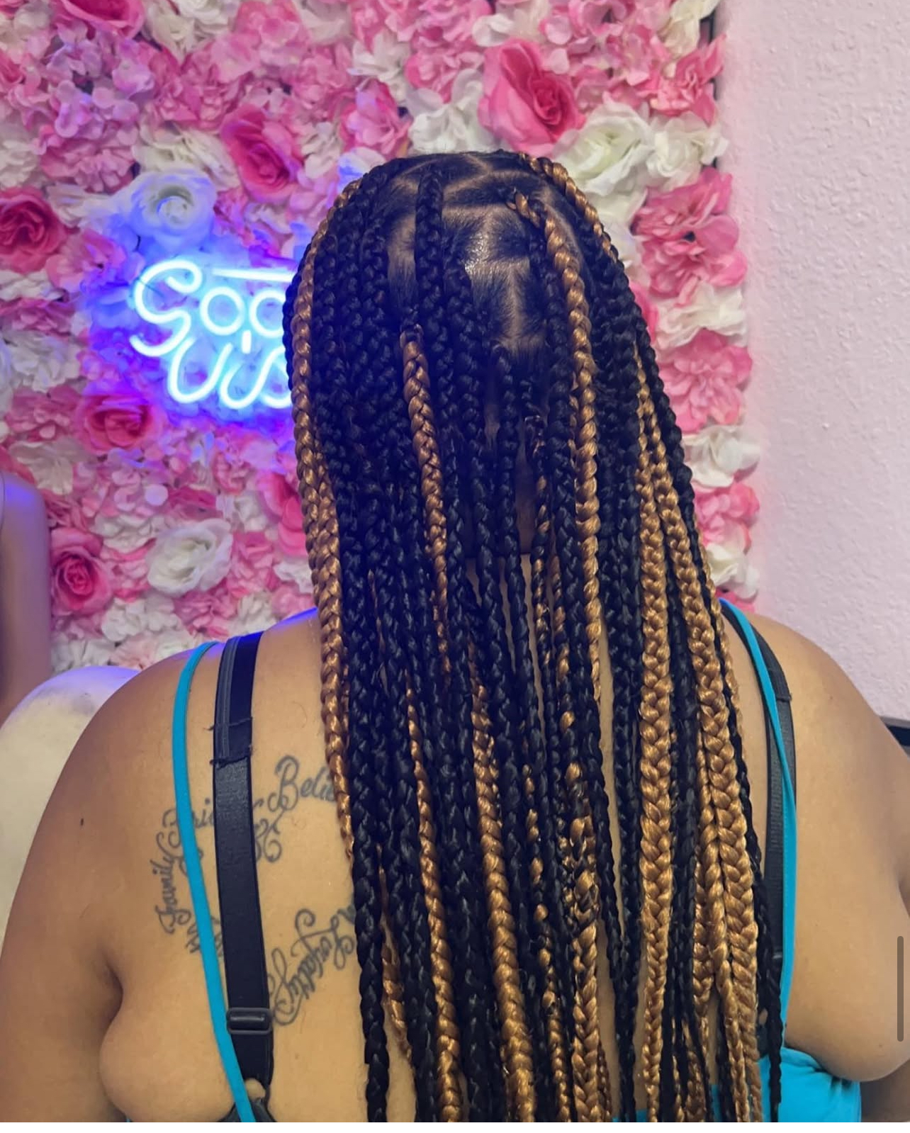 Mixed black and golden-brown box braids with a neon 'Good Vibes' sign in the background