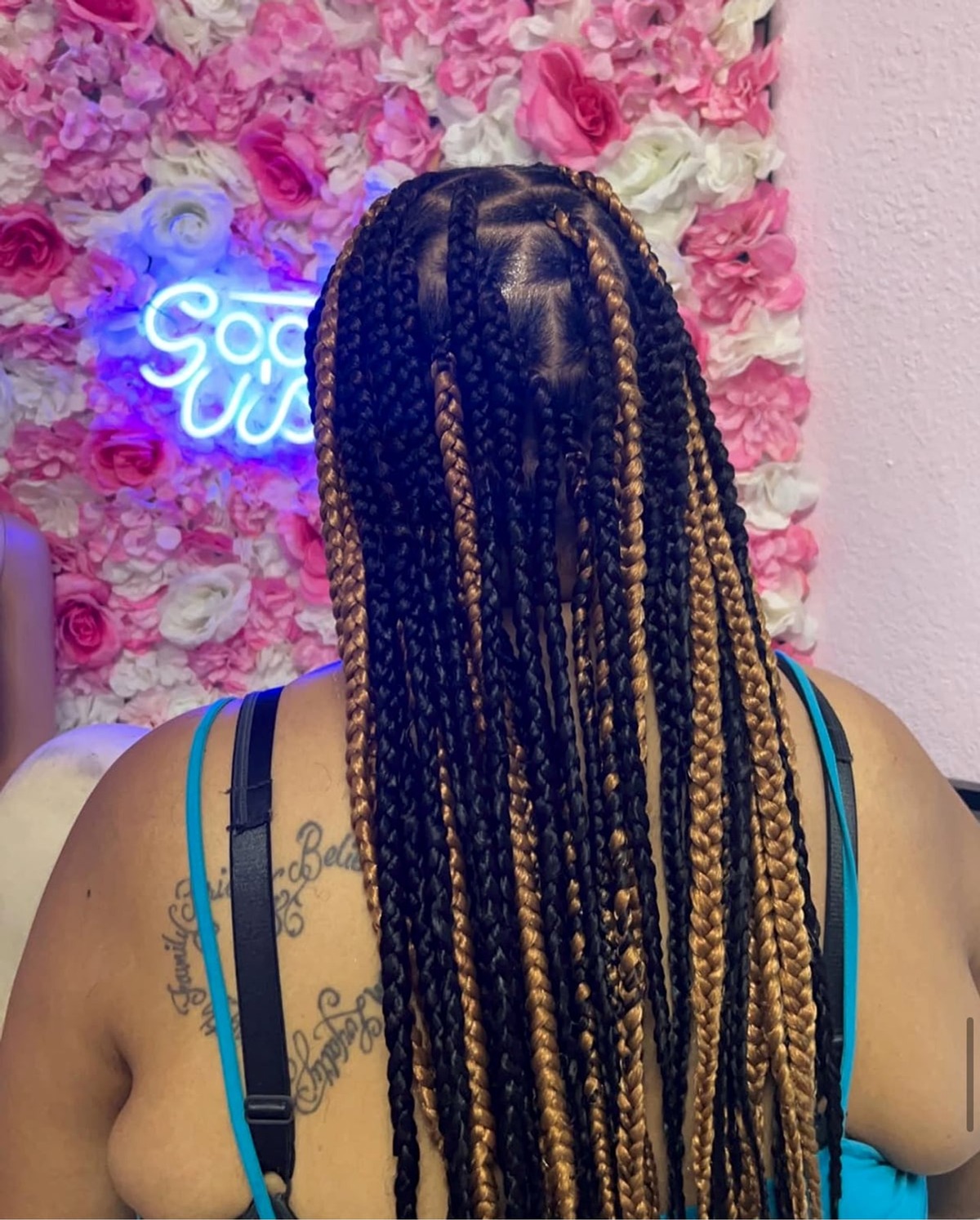 Mixed black and golden-brown box braids with a neon 'Good Vibes' sign in the background