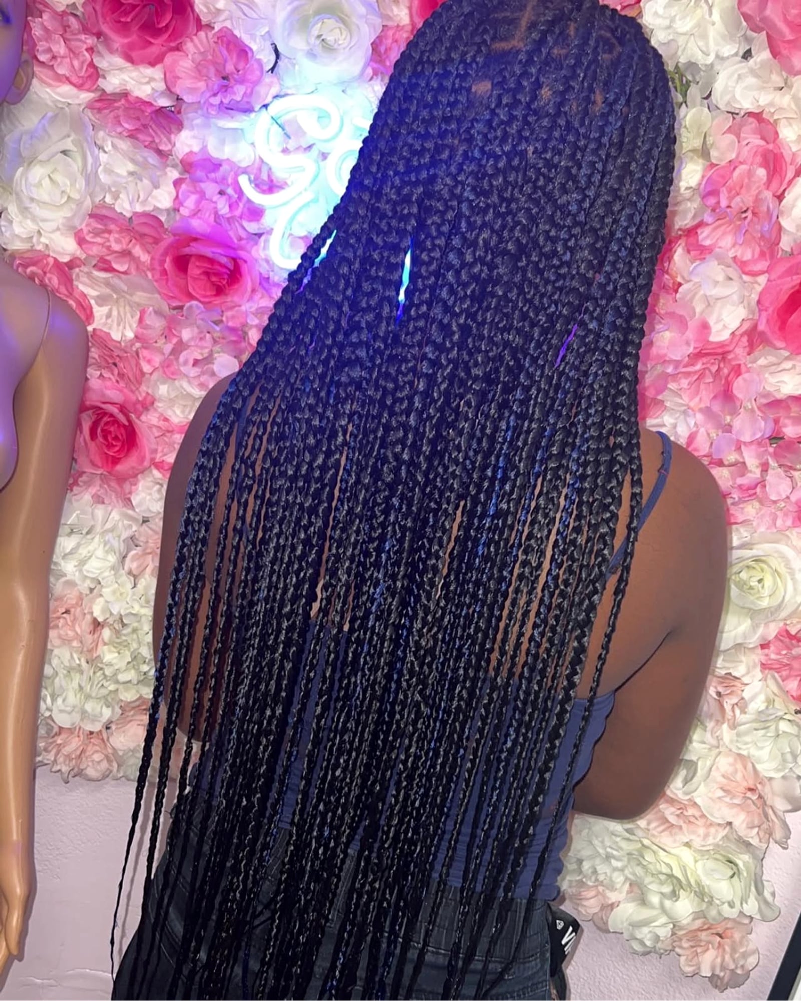 Long dark box braids with a neon 'Good Vibes' sign in the background